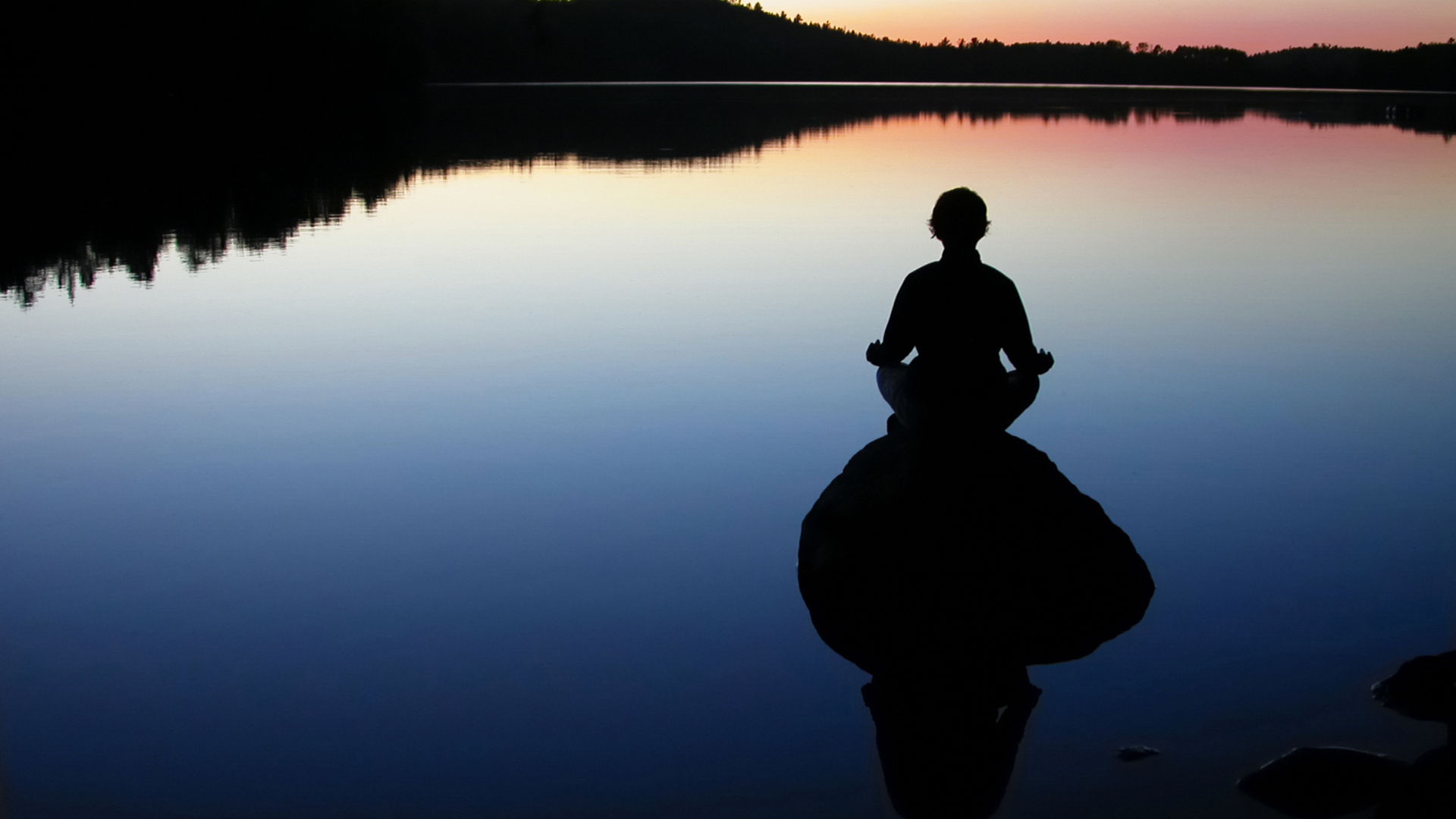 Person meditating on a rock in the middle of a lake